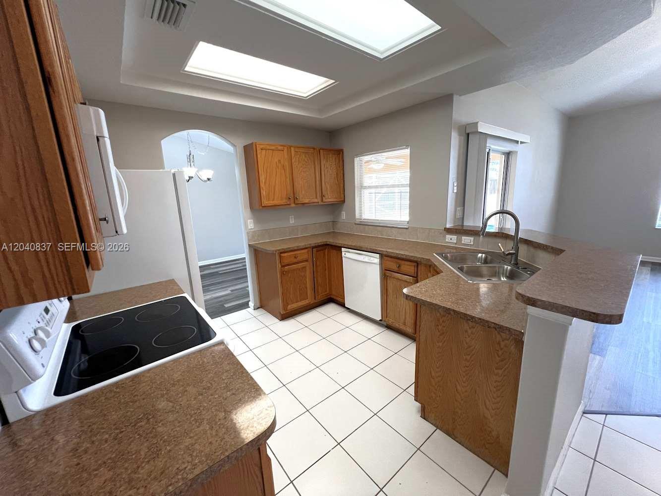 A kitchen features oak cabinets, laminate countertops, white appliances, and a tiled floor — PORT ST. LUCIE, FL