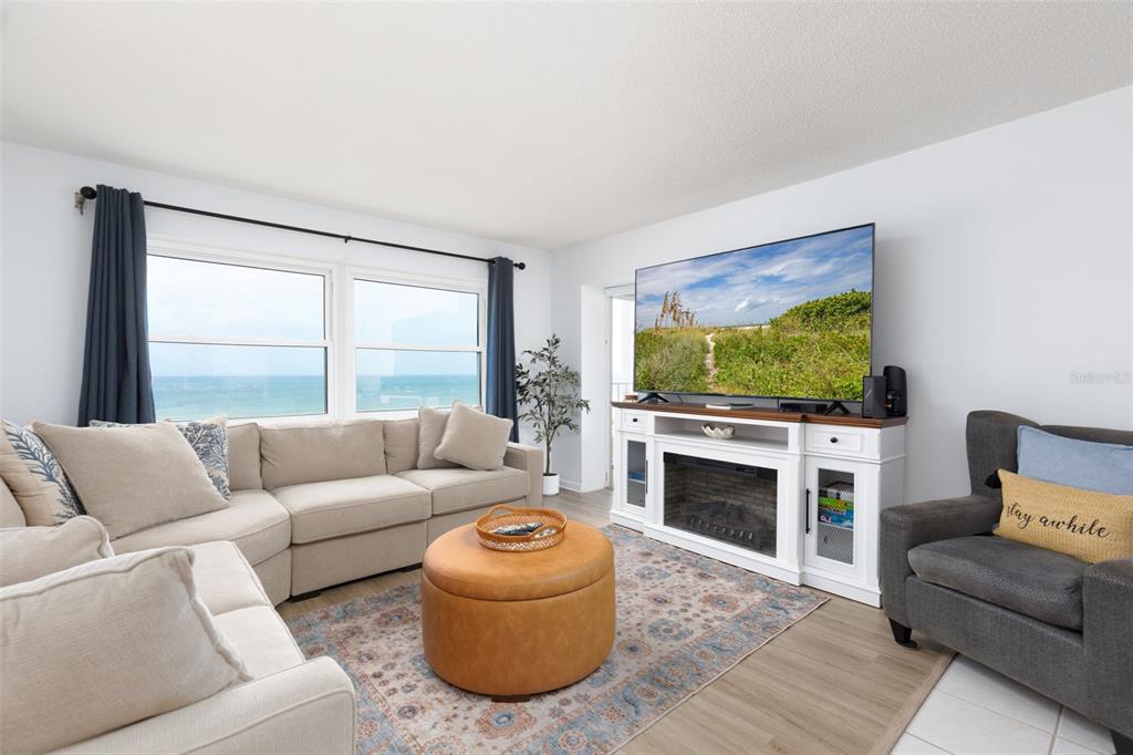 A living room features a beige sectional sofa, a round leather ottoman, and an ocean view — 11000 GULF BOULEVARD UNIT 1002, TREASURE ISLAND, FL