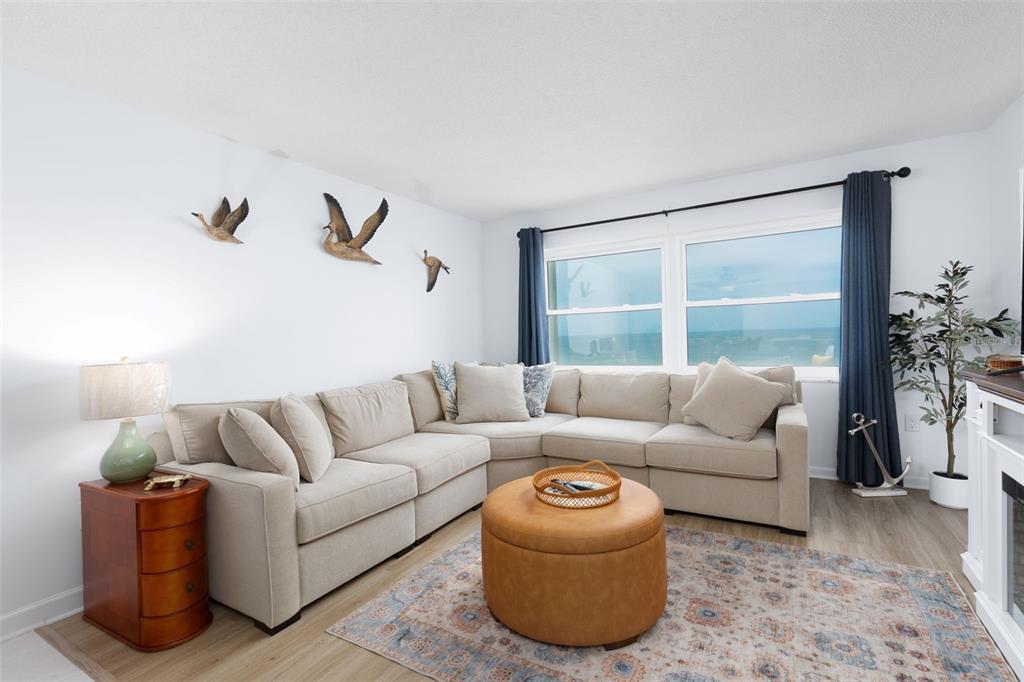 A living room features a beige sectional sofa, a round leather ottoman, and ocean views — 11000 GULF BOULEVARD UNIT 1002, TREASURE ISLAND, FL