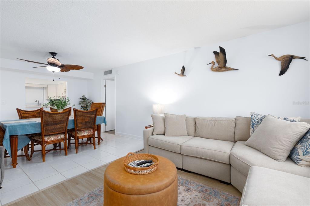 A living room features a beige sectional sofa, a round leather ottoman, and a dining area — 11000 GULF BOULEVARD UNIT 1002, TREASURE ISLAND, FL