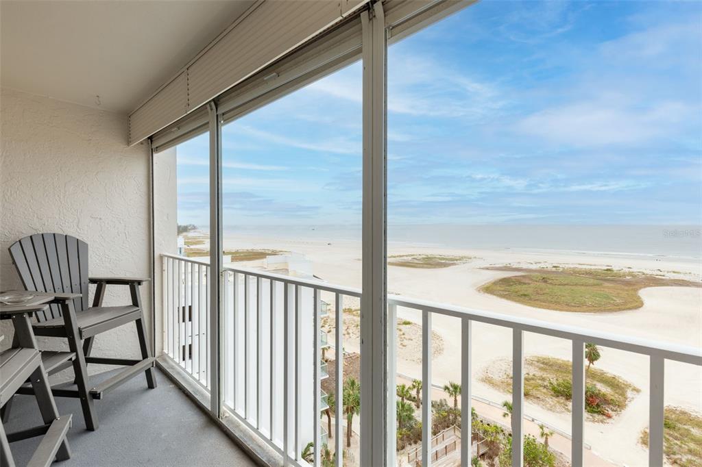 A balcony with a gray chair overlooks a sandy beach and the ocean — 11000 GULF BOULEVARD UNIT 1002, TREASURE ISLAND, FL