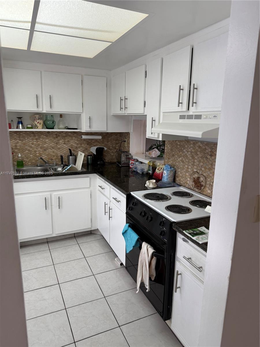 A galley kitchen features white cabinets, dark countertops, a black stove, and tiled flooring — 18555 NE 14th Ave # 618, Miami FL 33179, MIAMI, FL