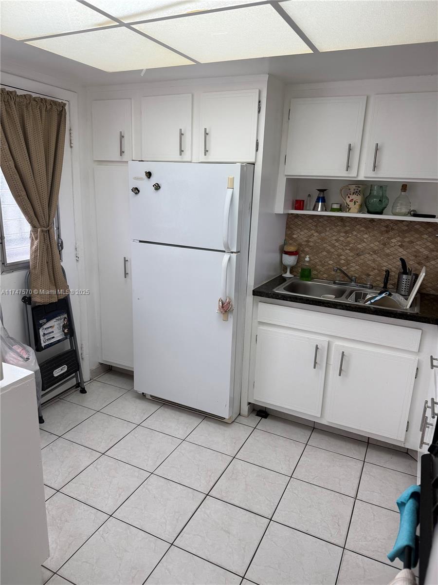 A kitchen features white cabinets, a white refrigerator, a double sink, and tiled flooring — 18555 NE 14th Ave # 618, Miami FL 33179, MIAMI, FL