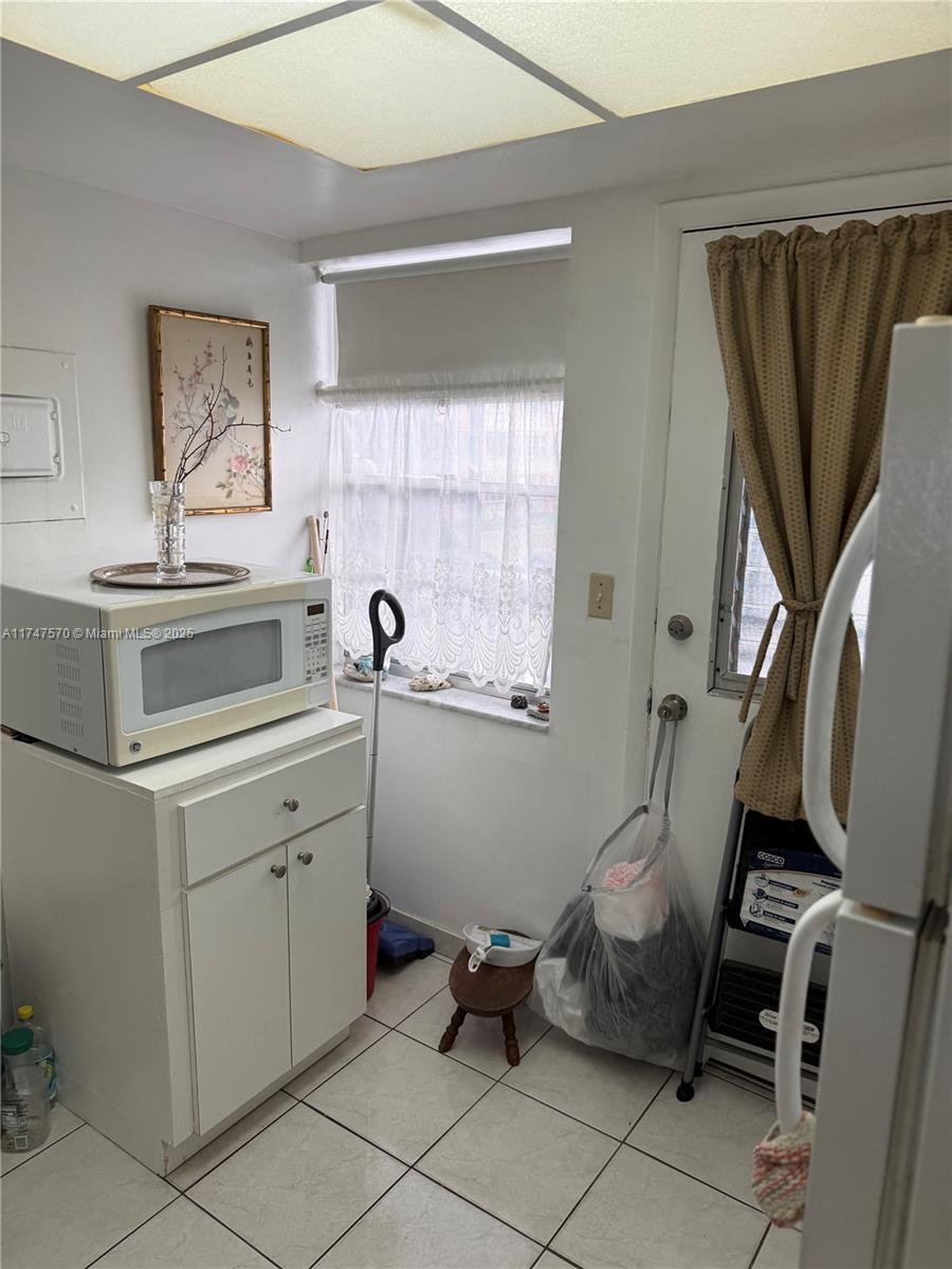 A kitchen area features white cabinets, a microwave, a window with curtains, and tile flooring — 18555 NE 14th Ave # 618, Miami FL 33179, MIAMI, FL