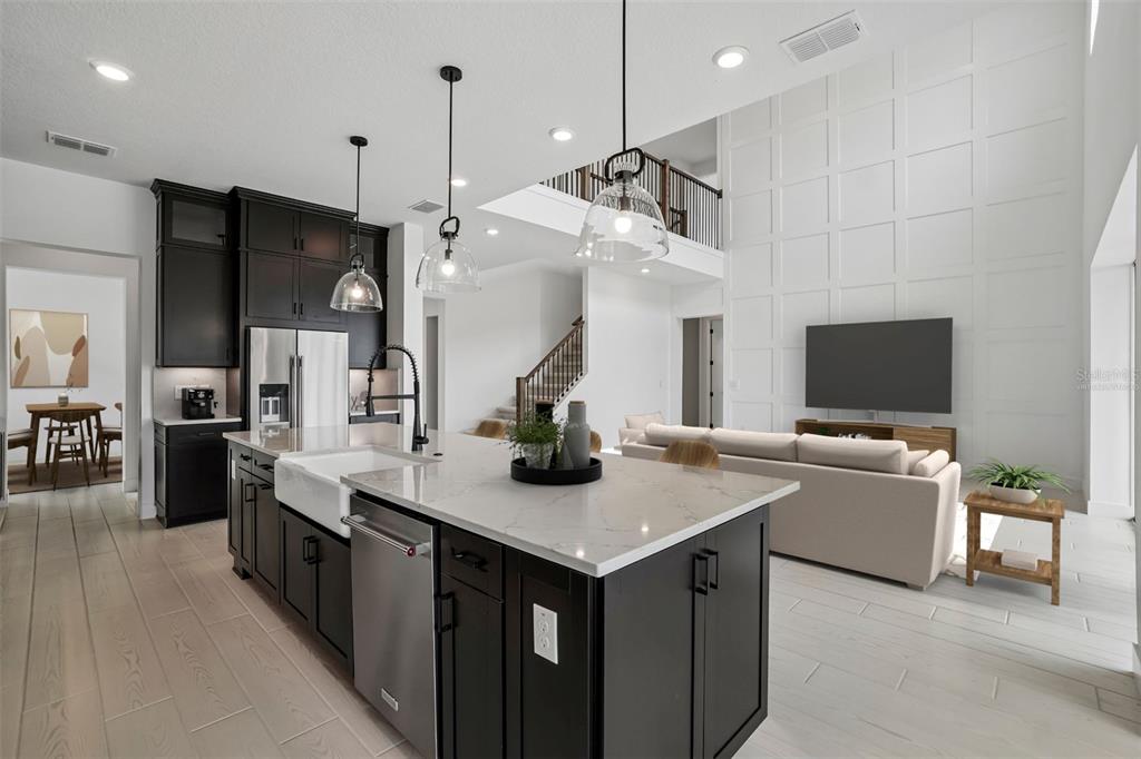 A modern kitchen with dark cabinets, a white quartz island, and an open-concept living area — 34960 BLAINE PASS, ZEPHYRHILLS, FL