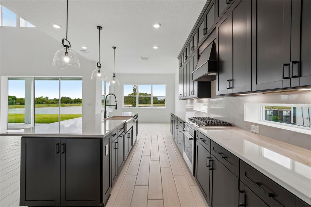 A modern kitchen features dark cabinetry, white countertops, stainless steel appliances, and a lake view — 34960 BLAINE PASS, ZEPHYRHILLS, FL