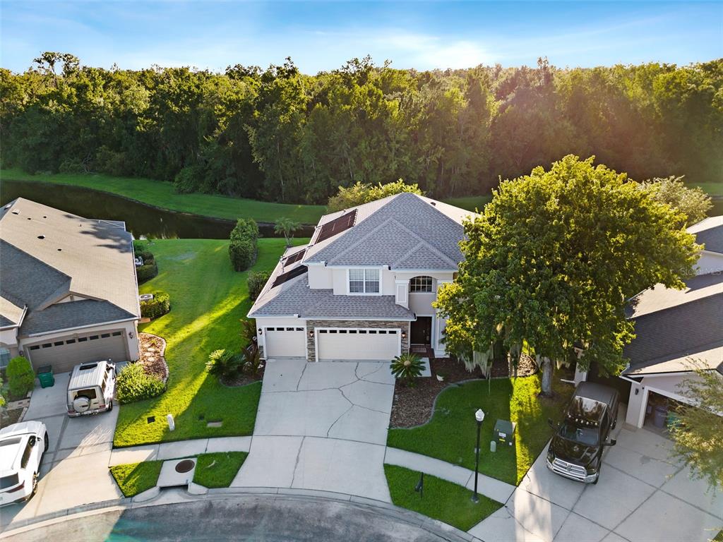 An aerial view shows a two-story house with a three-car garage and solar panels — 27015 FIREBUSH DRIVE, WESLEY CHAPEL, FL