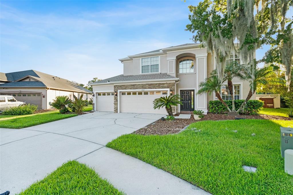 A two-story suburban house with a stone-accented facade, a three-car garage, and a landscaped lawn — 27015 FIREBUSH DRIVE, WESLEY CHAPEL, FL