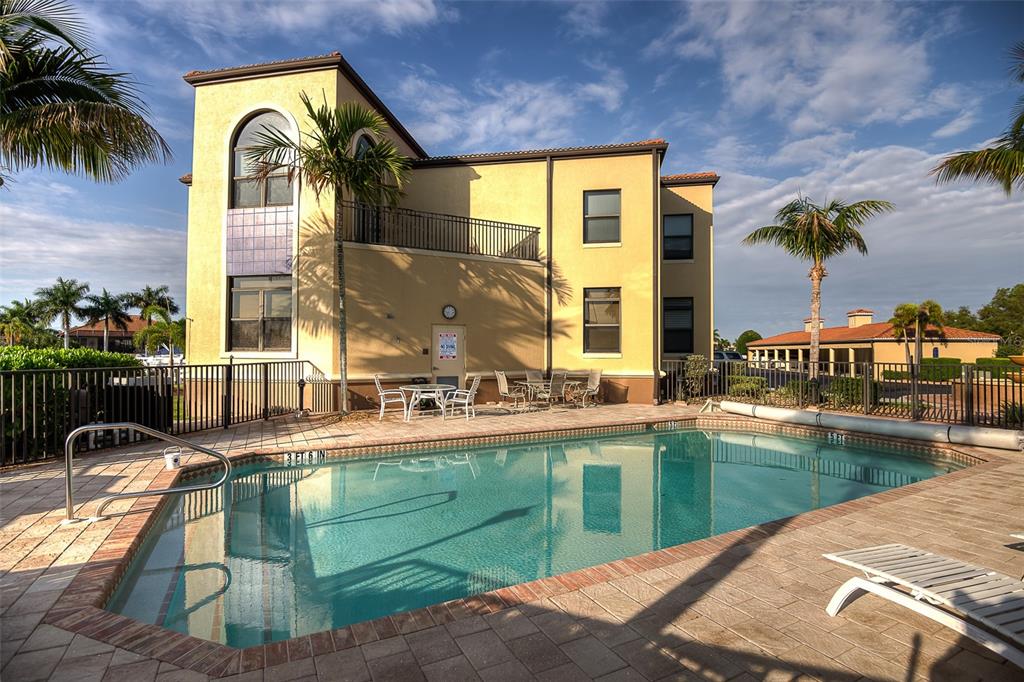 A swimming pool sits on a paved patio in front of a multi-story yellow building — 3334 PURPLE MARTIN DRIVE UNIT 212, PUNTA GORDA, FL