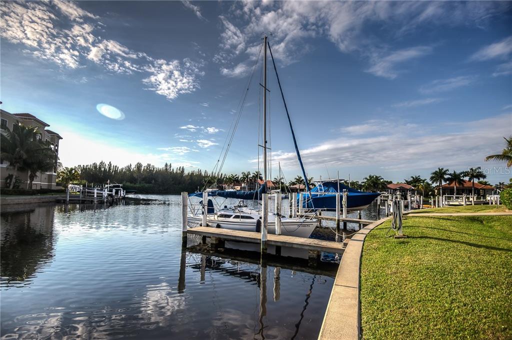 A sailboat is docked at a wooden pier along a canal near residential buildings — 3334 PURPLE MARTIN DRIVE UNIT 212, PUNTA GORDA, FL