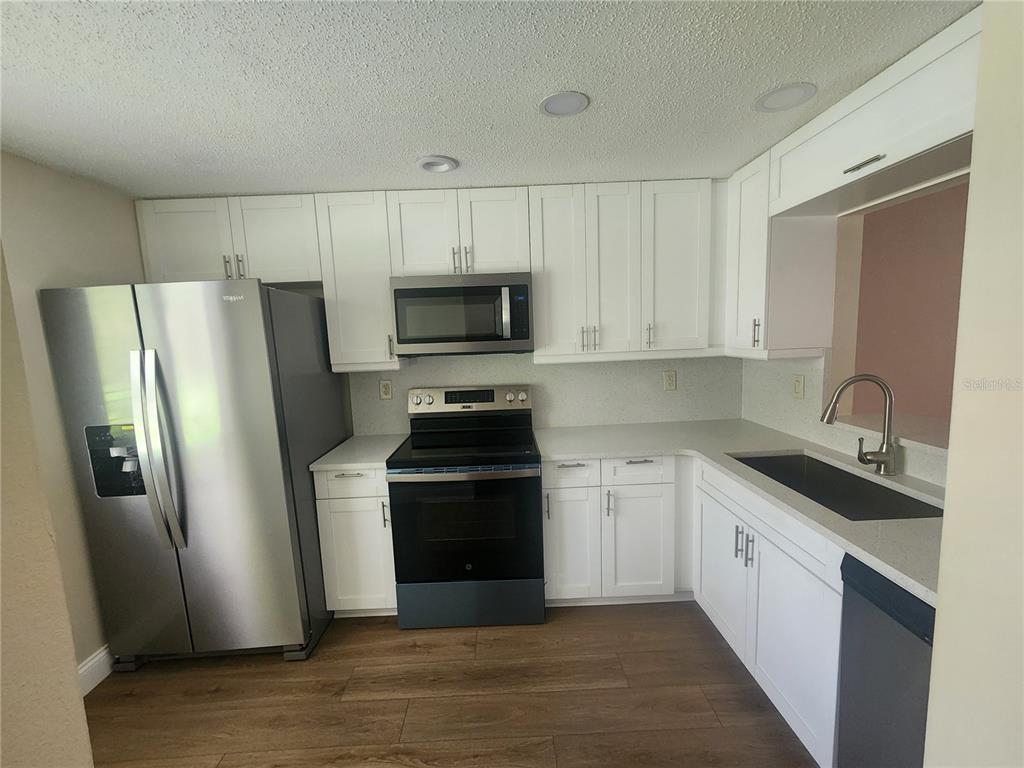 A kitchen features white cabinets, stainless steel appliances, a dark sink, and wood-look flooring — 209 CORKWOOD LN, OLDSMAR, FL
