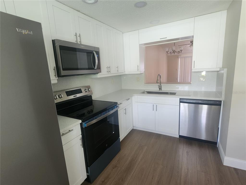 A kitchen features white cabinets, stainless steel appliances, quartz countertops, and wood-look flooring — 209 CORKWOOD LN, OLDSMAR, FL