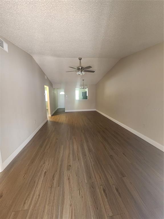 A long, empty living room features light wood-look flooring, beige walls, and a ceiling fan — 209 CORKWOOD LN, OLDSMAR, FL