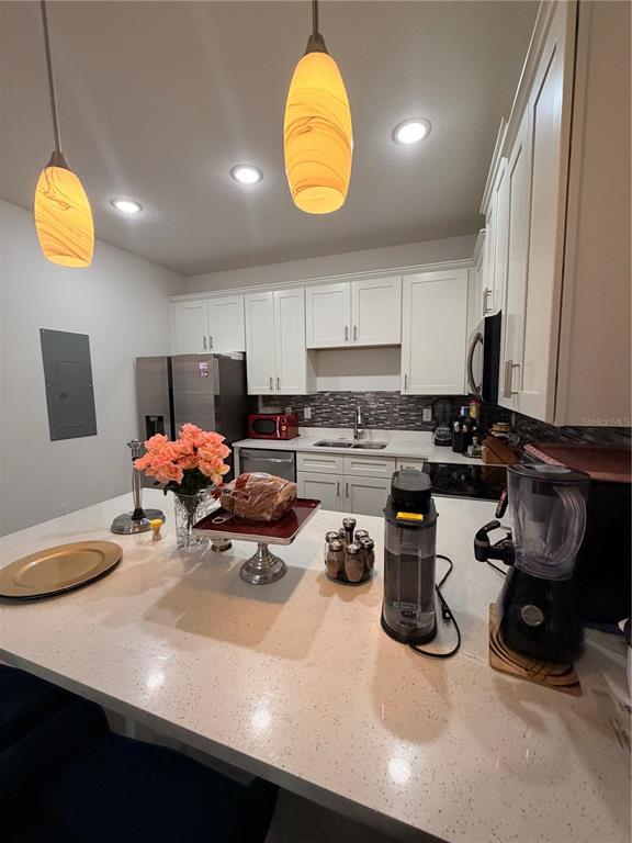 A kitchen features white cabinets, quartz countertops, stainless steel appliances, and two pendant lights — 1615 CUMIN DRIVE, POINCIANA, FL