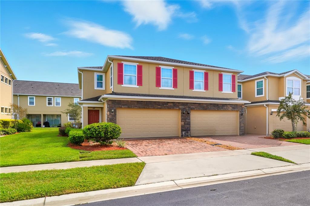 A two-story townhouse with a tan stucco exterior, stone accents, and two garage doors — 1617 MOHEGAN BOULEVARD, KISSIMMEE, FL
