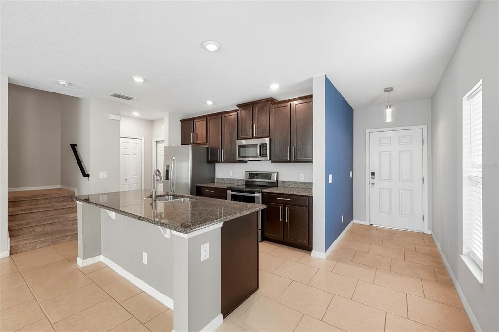 A kitchen with dark wood cabinets, granite countertops, and an island, adjacent to an entryway — 1617 MOHEGAN BOULEVARD, KISSIMMEE, FL
