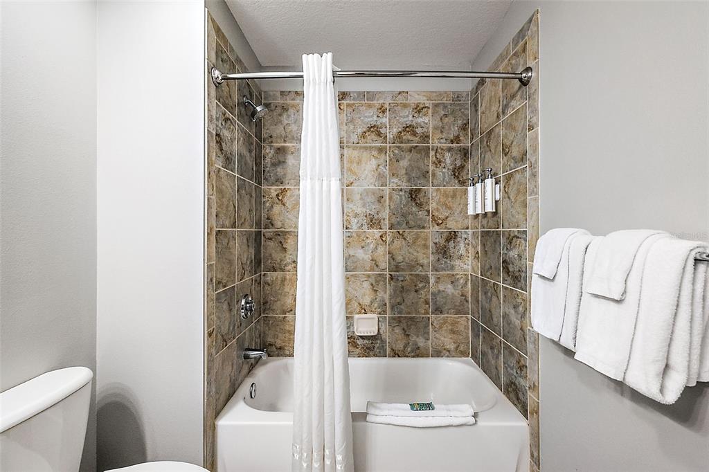 A bathroom features a white bathtub with a shower, tiled walls, and white towels — 14501 GROVE RESORT AVENUE UNIT 1614, WINTER GARDEN, FL
