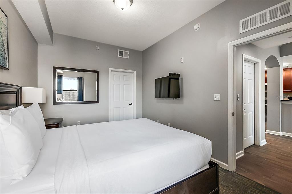 A bedroom with a white bed, gray walls, a wall-mounted television, and an adjacent doorway — 14501 GROVE RESORT AVENUE UNIT 1614, WINTER GARDEN, FL