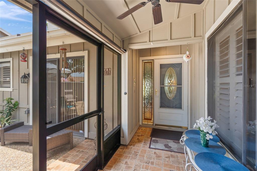 A covered porch features a tiled floor, a ceiling fan, and a glass-paneled front door — 4562 FOREST WOOD TRAIL UNIT 15, SARASOTA, FL