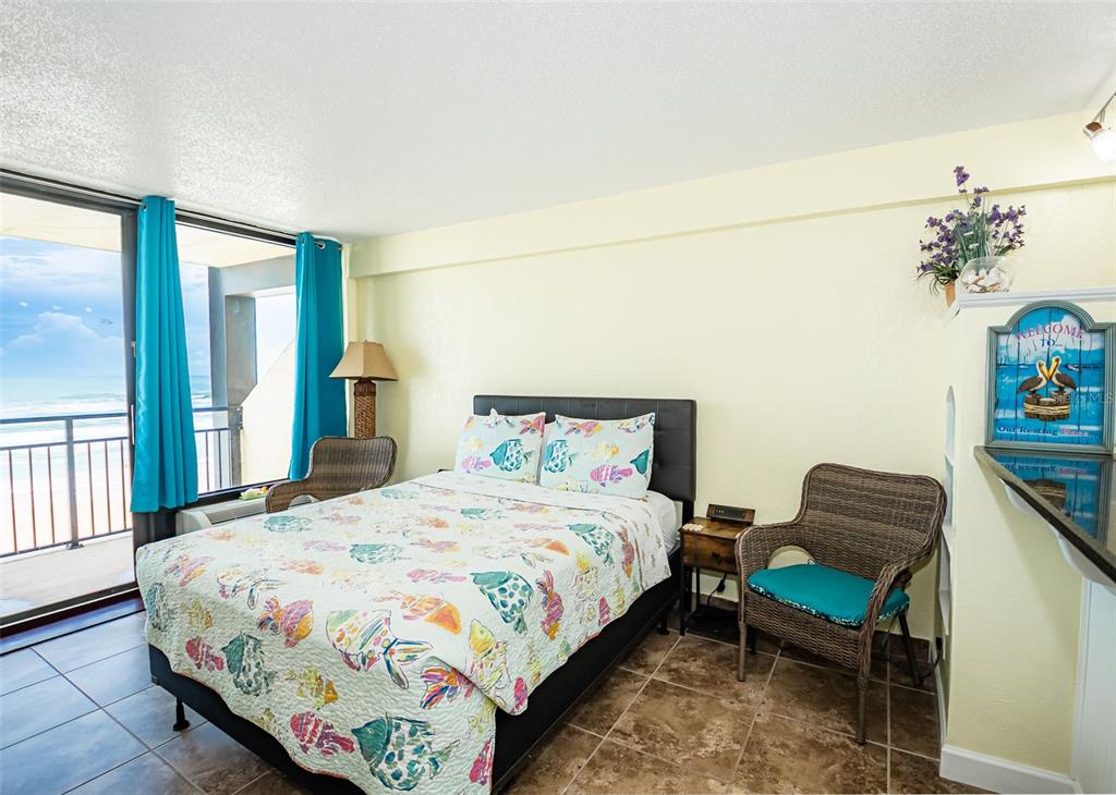 A bedroom with a fish-patterned quilt, wicker chairs, and a balcony overlooking the ocean — 2301 S ATLANTIC AVENUE UNIT 435, DAYTONA BEACH, FL
