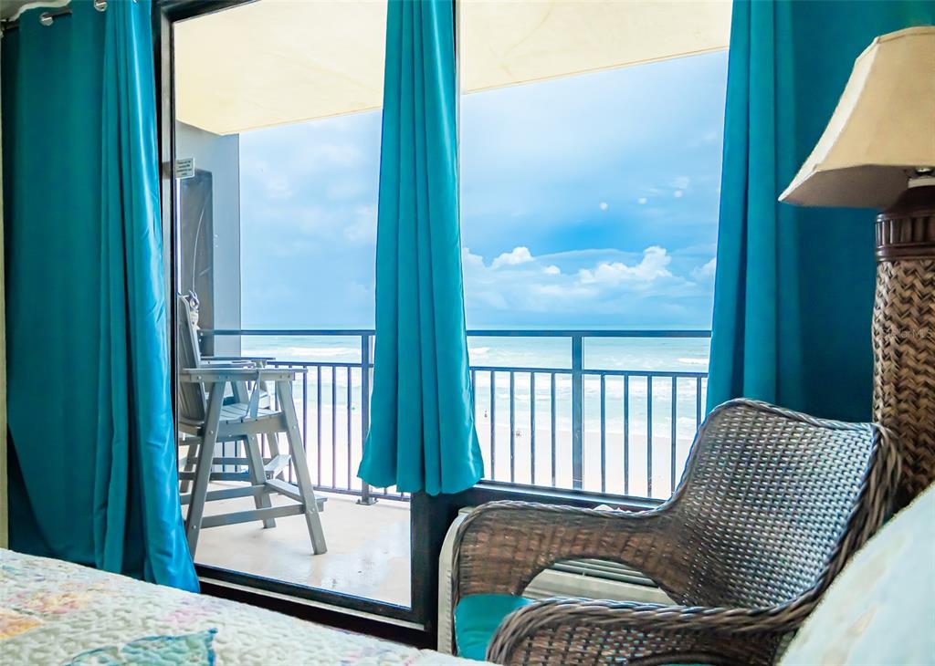 A bedroom with a wicker chair and curtains overlooking a balcony with an ocean view — 2301 S ATLANTIC AVENUE UNIT 435, DAYTONA BEACH, FL