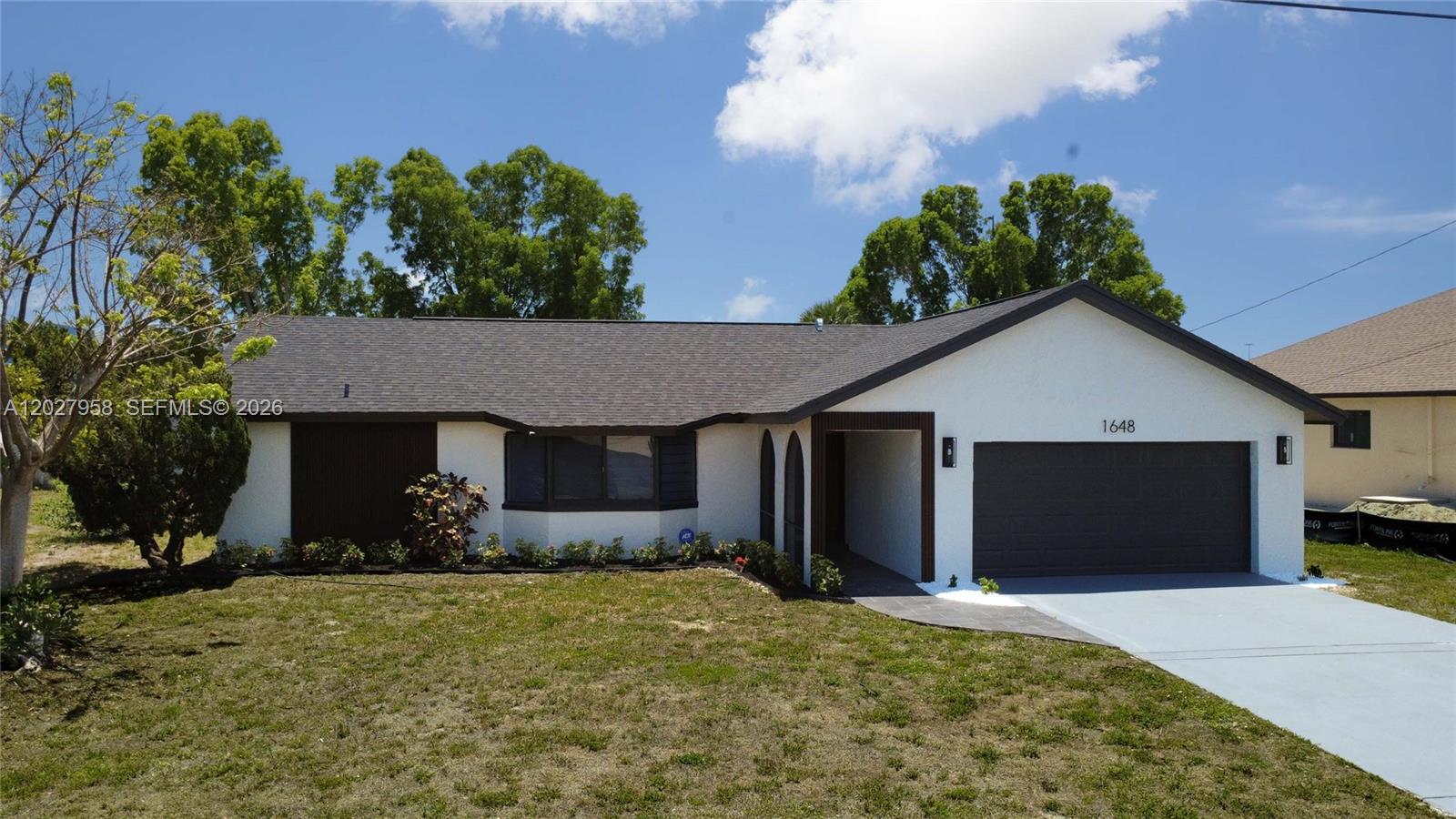 A single-story house with a white stucco facade, dark trim, and a two-car garage — 1648 Coral Point Dr, Cape Coral FL 33990, CAPE CORAL, FL