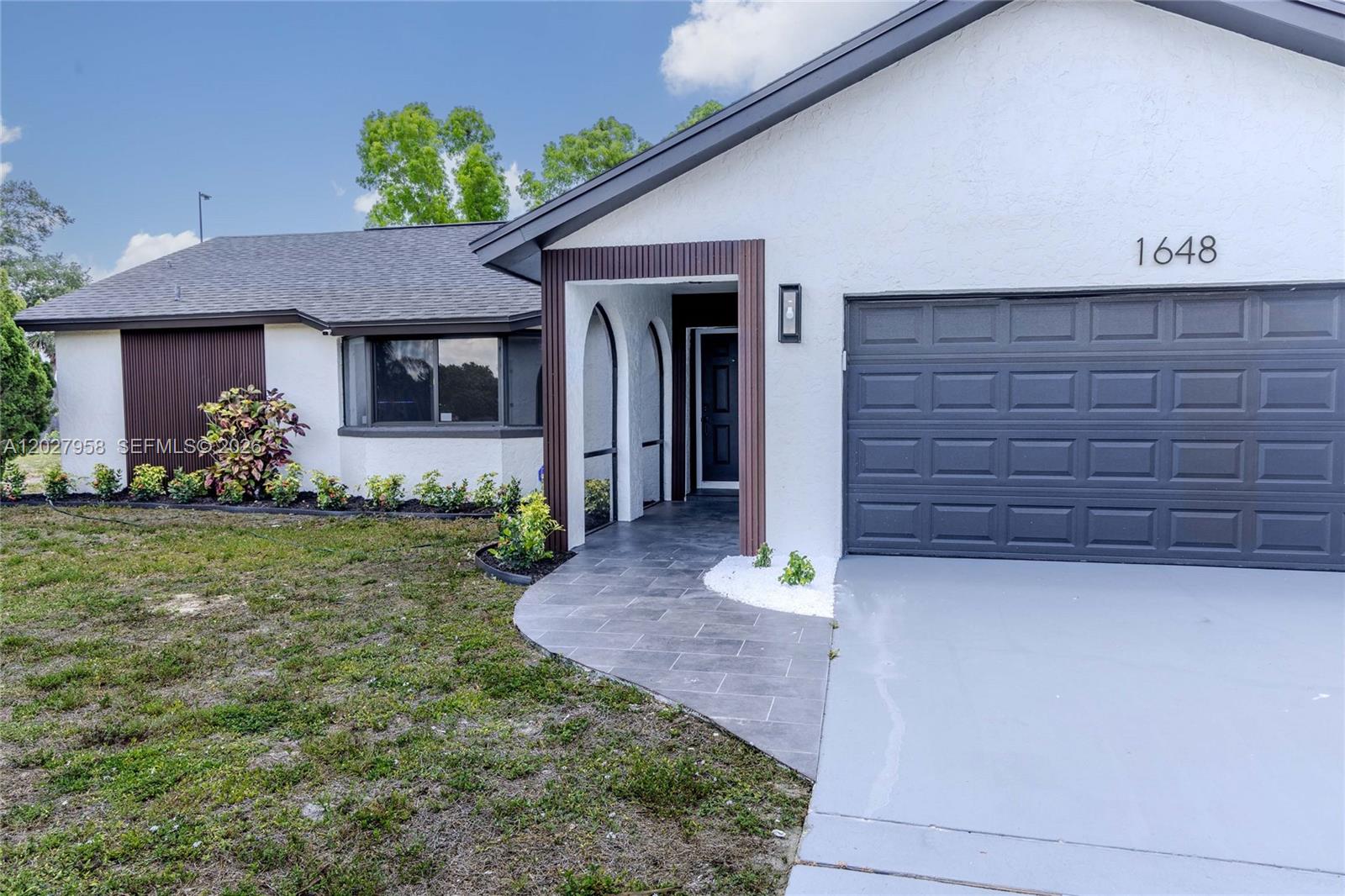 The exterior of a single-story house features a gray garage door and a covered entryway — 1648 Coral Point Dr, Cape Coral FL 33990, CAPE CORAL, FL