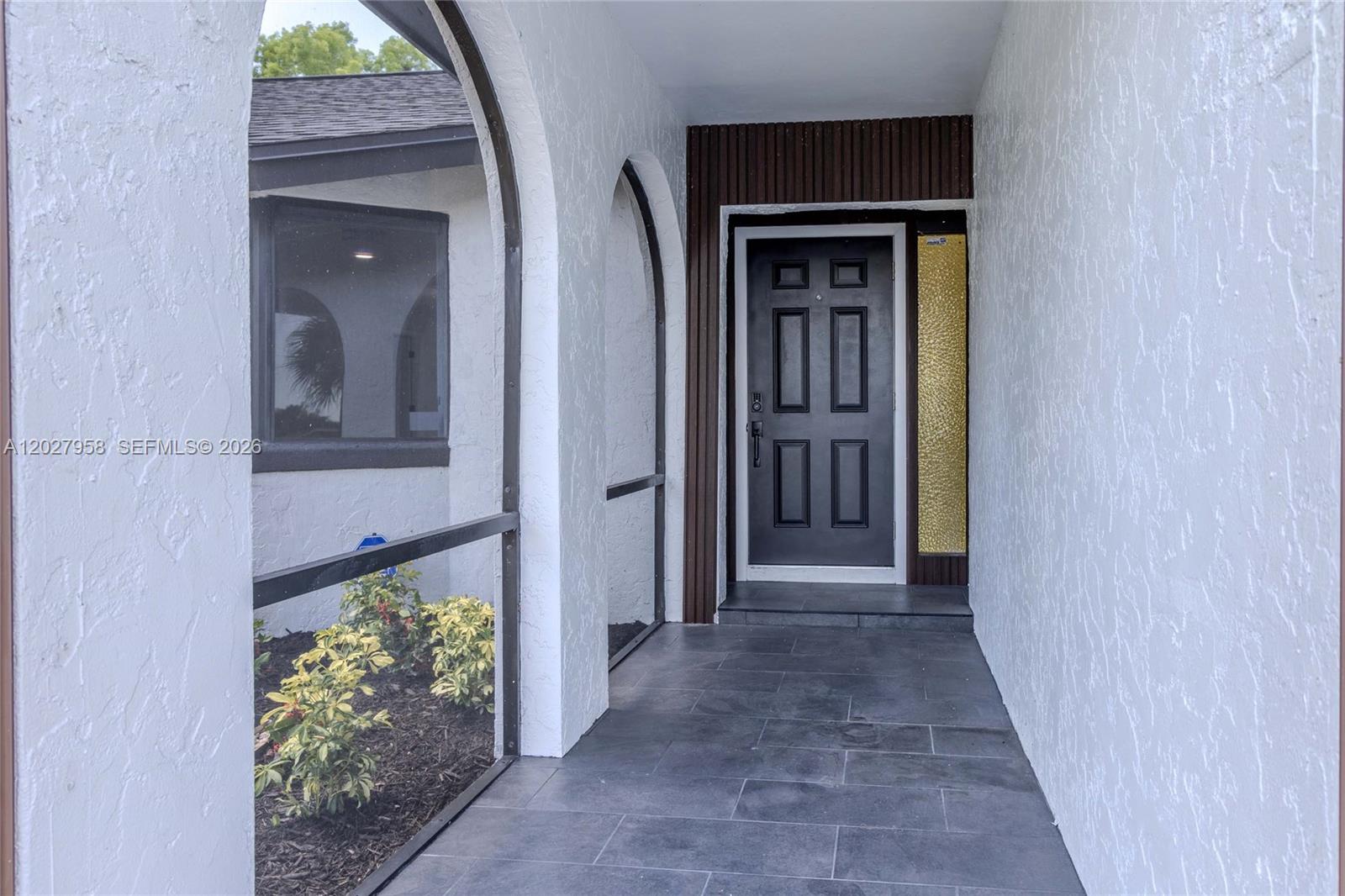 A covered entryway features white arched walls, a dark front door, and gray tile flooring — 1648 Coral Point Dr, Cape Coral FL 33990, CAPE CORAL, FL