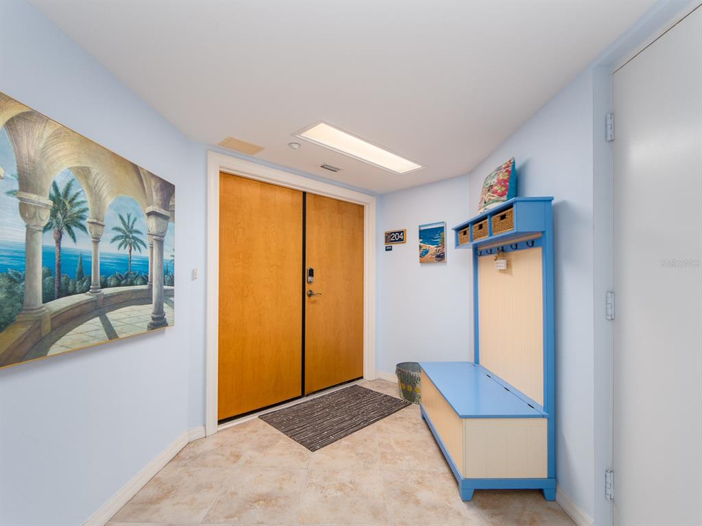 An entryway features light blue walls, tile flooring, a wooden double door, and a storage bench — 1370 GULF BOULEVARD UNIT 204, CLEARWATER, FL