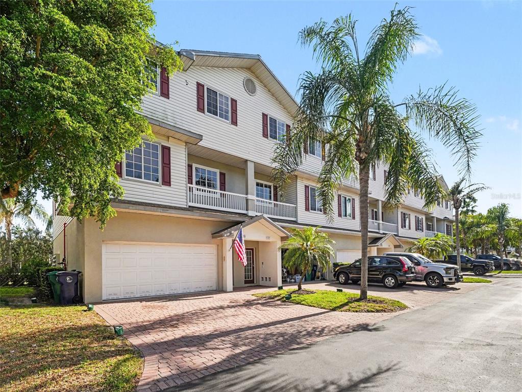 A three-story townhouse with white siding, a two-car garage, and a brick paver driveway — 3325 10TH LANE W, PALMETTO, FL