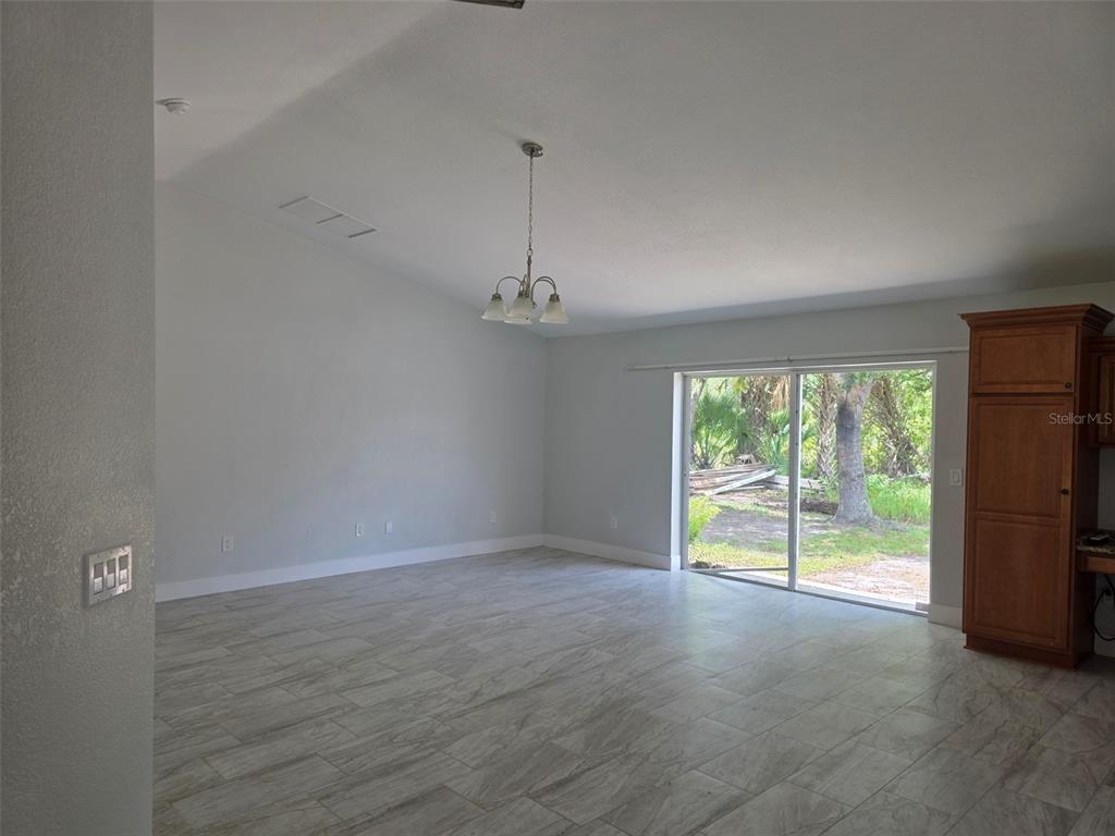 A living area with light gray walls, tile flooring, a chandelier, and a sliding glass door — 3291 HORACE AVENUE, NORTH PORT, FL
