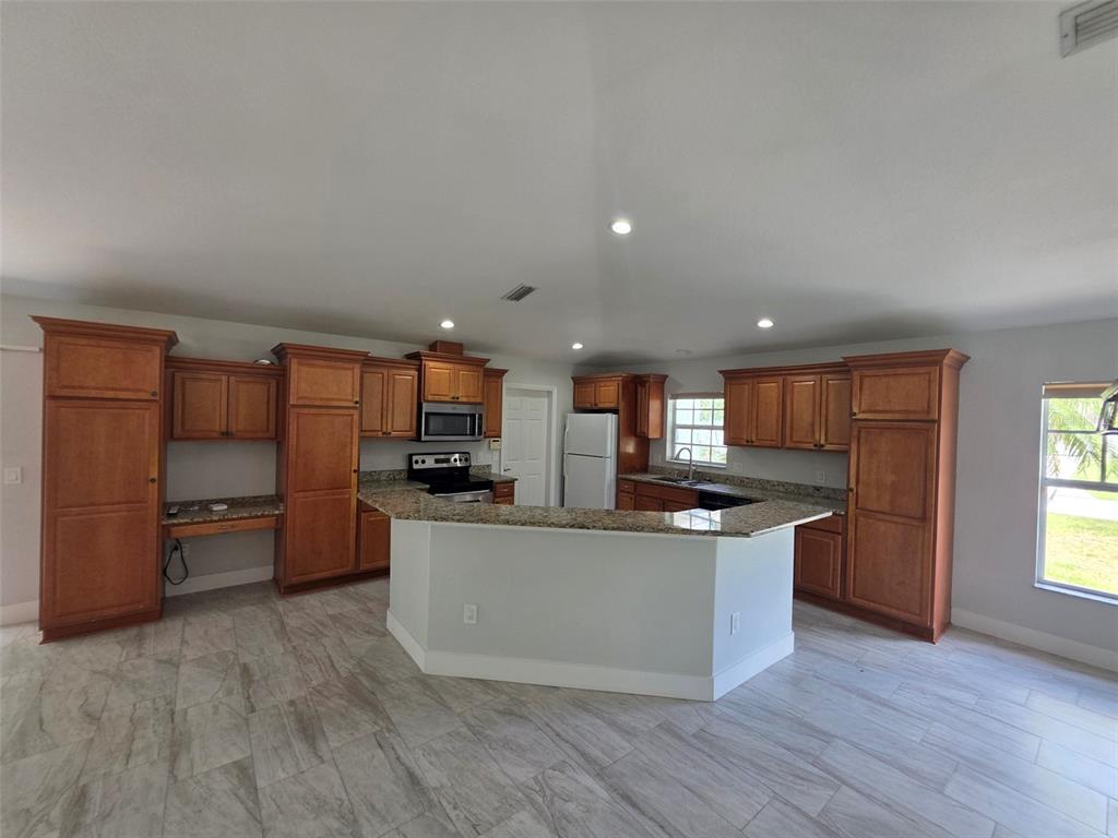 A kitchen features wood cabinetry, granite countertops, a peninsula, and light-colored tile flooring — 3291 HORACE AVENUE, NORTH PORT, FL