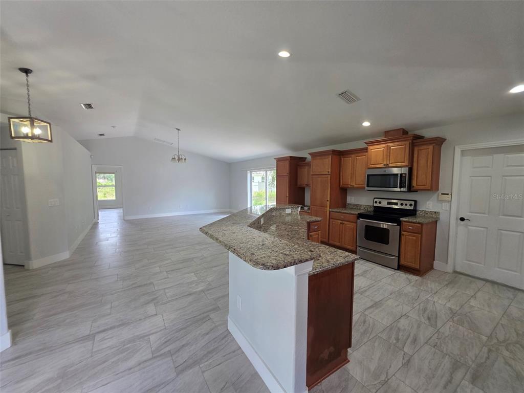 An open-concept kitchen with granite countertops and wood cabinets overlooks a spacious living area — 3291 HORACE AVENUE, NORTH PORT, FL