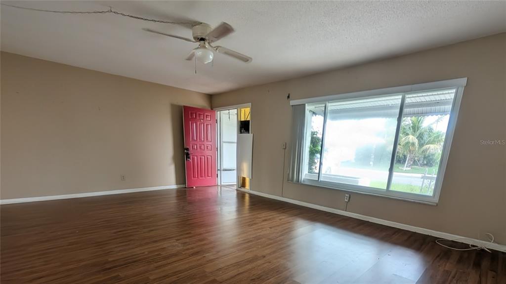 A living room with wood-look flooring, a ceiling fan, a red door, and large windows — 9640 45TH STREET N, PINELLAS PARK, FL