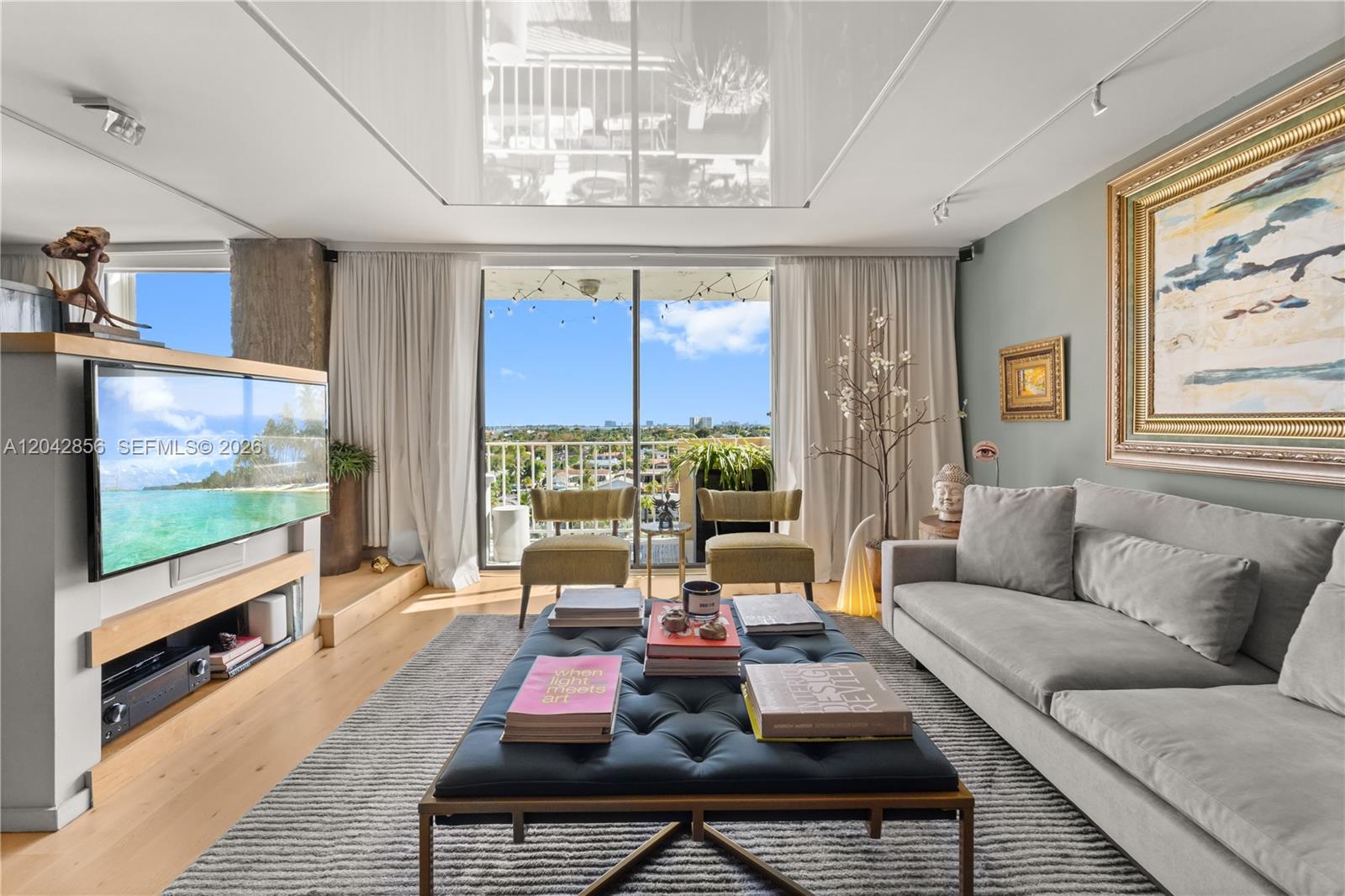A living room features a tufted ottoman, gray sofa, television, and a balcony with views — 2350 NE 135th St # 808, North Miami FL 33181, NORTH MIAMI, FL