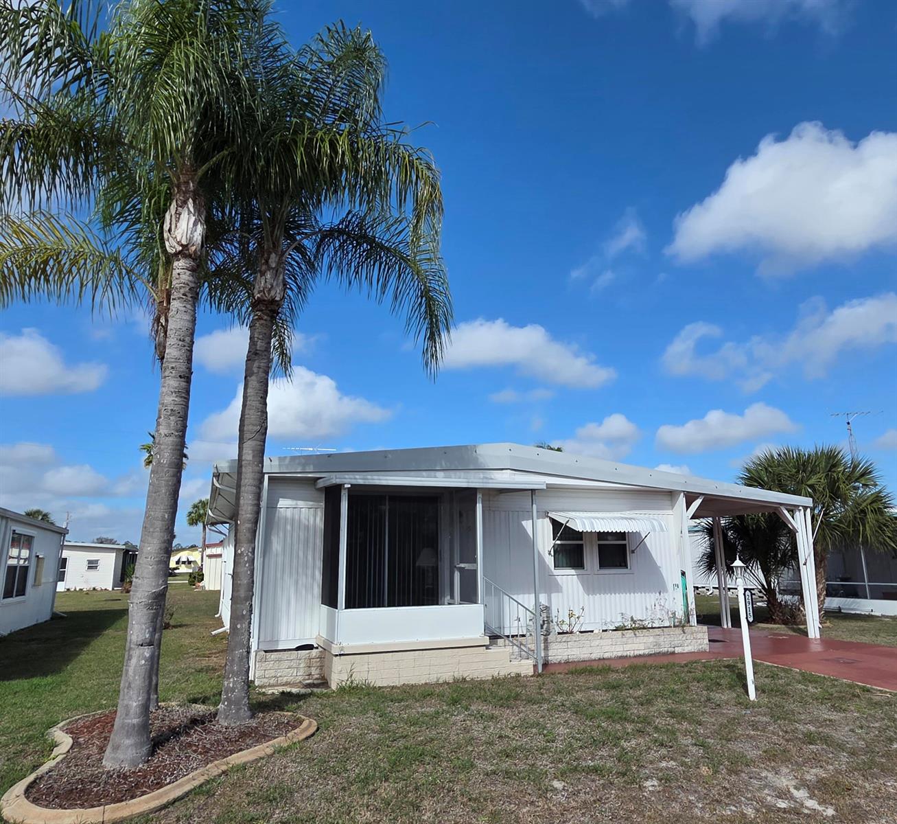 A white mobile home with a screened porch, palm trees, and a carport — 2915 Roger Street, Sebring FL 33872, SEBRING, FL