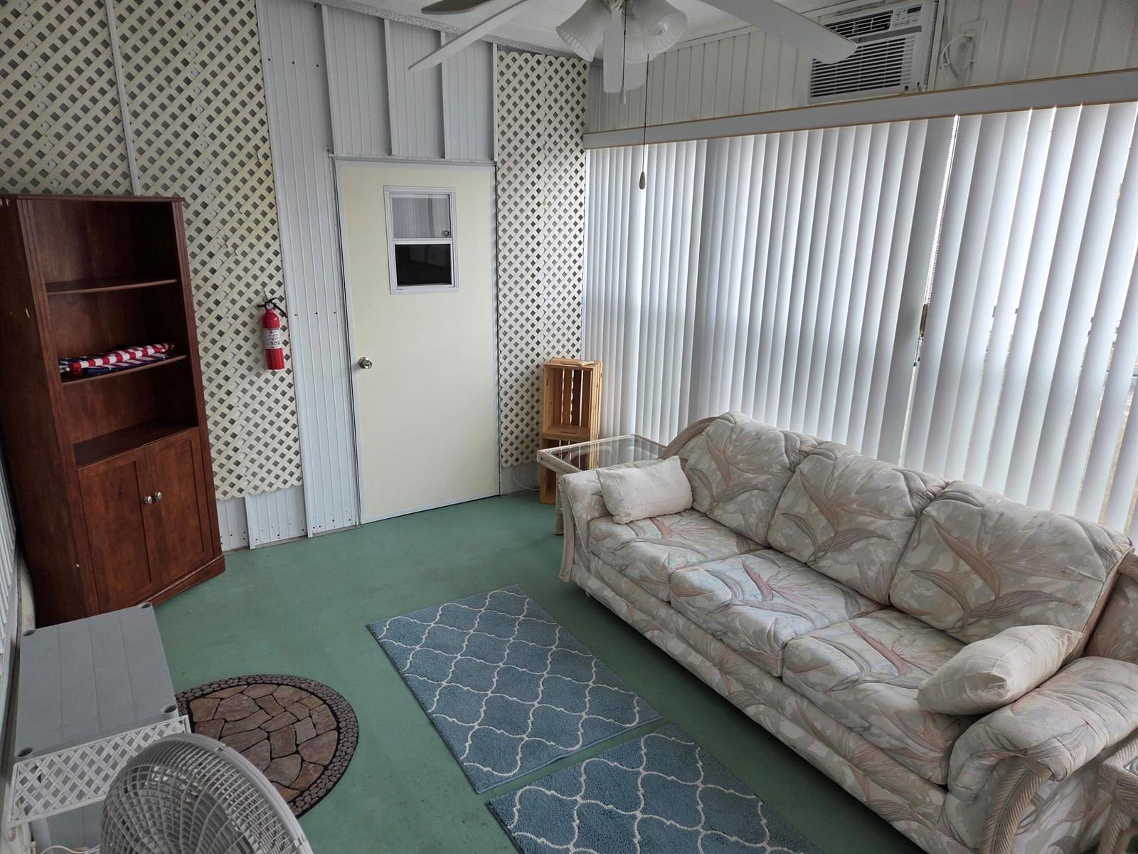 A sunroom features a floral sofa, green flooring, lattice wall panels, and vertical window blinds — 2915 Roger Street, Sebring FL 33872, SEBRING, FL