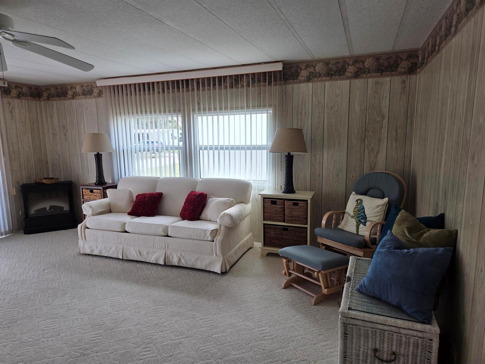 A living room features wood-paneled walls, a white sofa, a rocking chair, and vertical blinds — 2915 Roger Street, Sebring FL 33872, SEBRING, FL