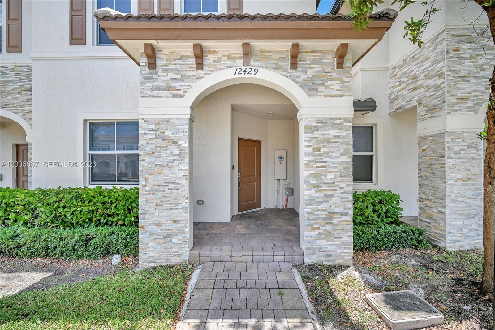 The exterior entrance features a stone-faced arched portico, a brown door, and a paver walkway — 12429 NW 23rd Ct, Miami FL 33167, MIAMI, FL