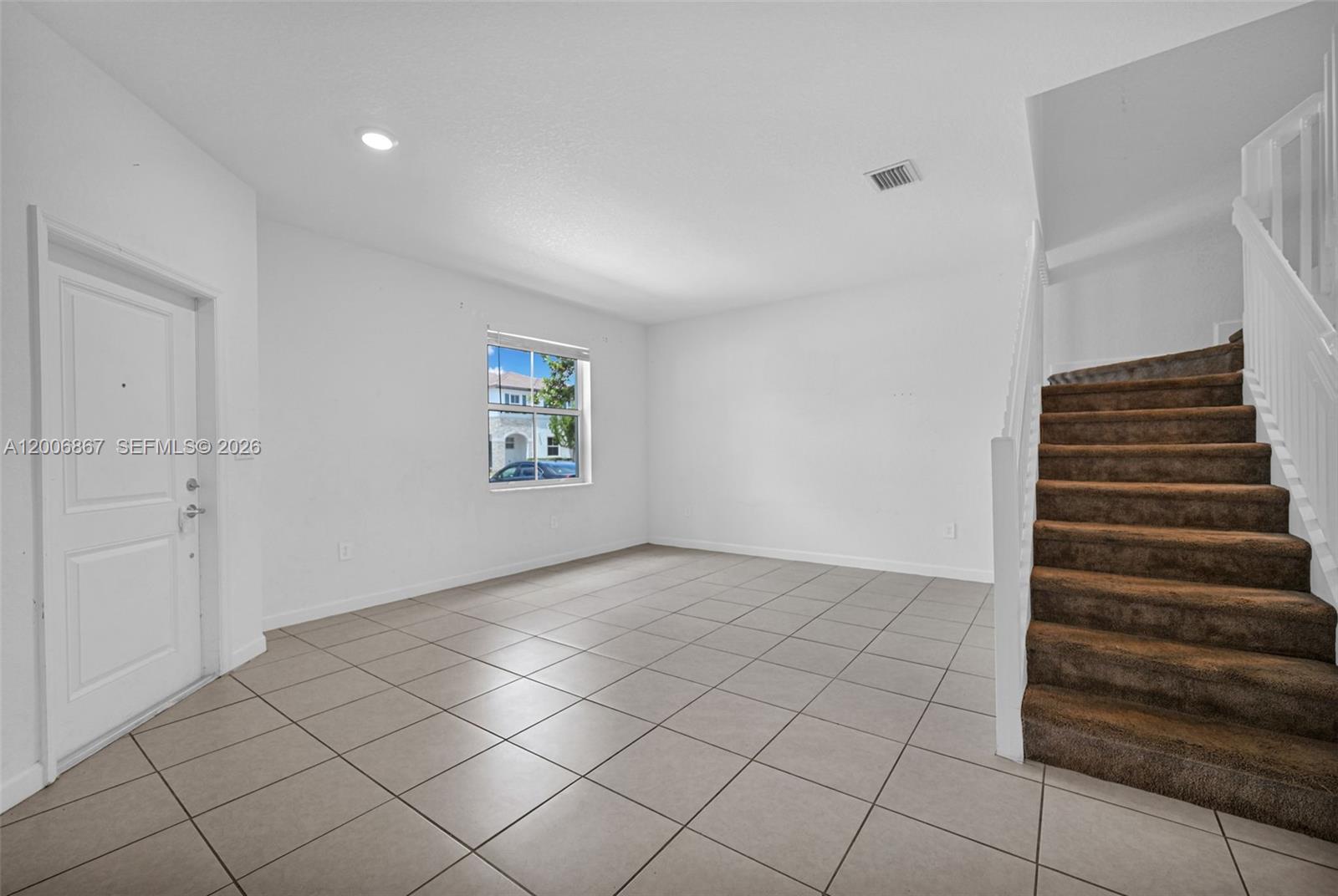 An empty room features white walls, tile flooring, a window, and a carpeted staircase — 12429 NW 23rd Ct, Miami FL 33167, MIAMI, FL