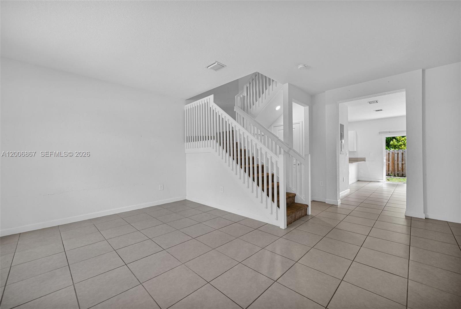 An empty room with light tile flooring features a white staircase and a doorway — 12429 NW 23rd Ct, Miami FL 33167, MIAMI, FL