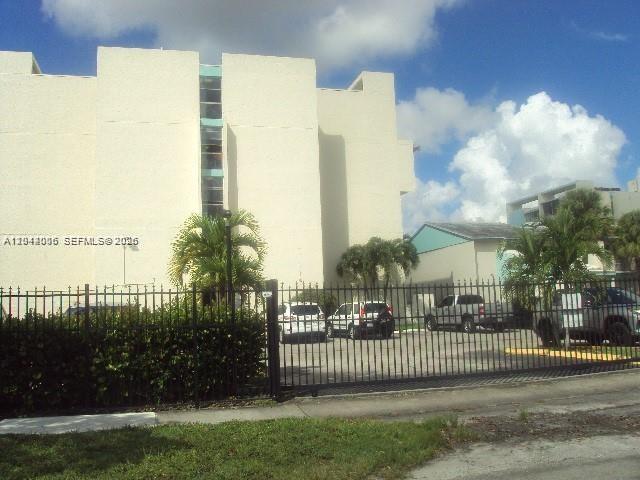 A multi-story beige apartment building stands behind a black metal fence and parking lot — 2017 NW 46th Ave # A406, Lauderhill FL 33313, LAUDERHILL, FL