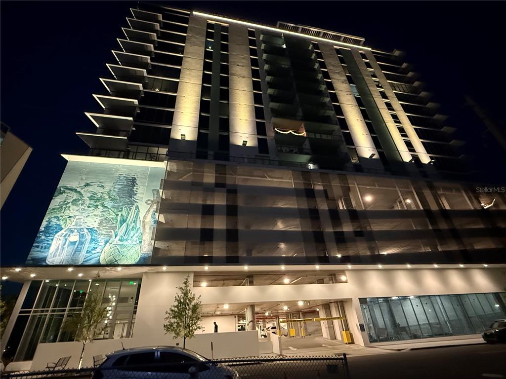 A low-angle night view of a modern high-rise building featuring a large mural — 777 3RD AVENUE N UNIT 908, ST PETERSBURG, FL