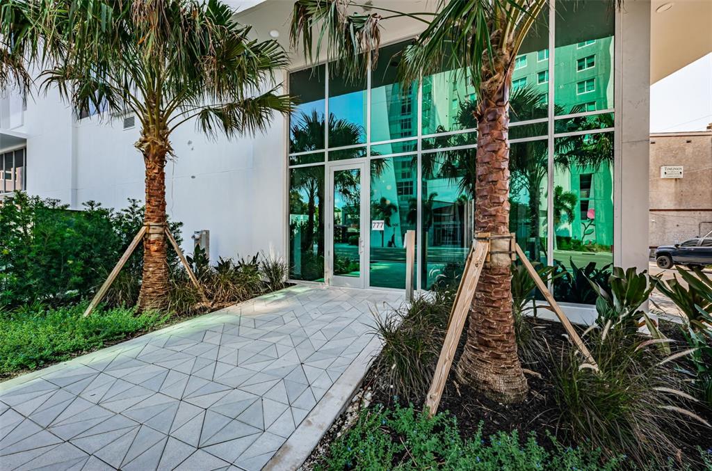 A modern building entrance features glass doors, large windows, and two palm trees with supports — 777 3RD AVENUE N UNIT 908, ST PETERSBURG, FL