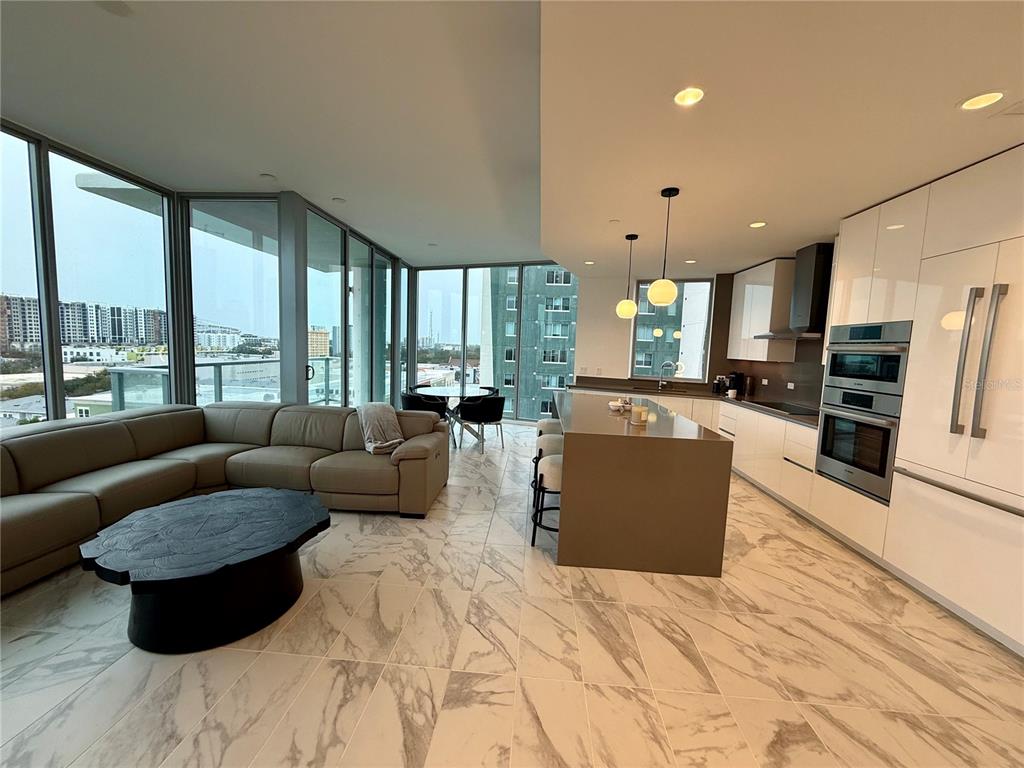 A modern open-concept living room and kitchen feature marble floors, floor-to-ceiling windows, and stainless appliances — 777 3RD AVENUE N UNIT 908, ST PETERSBURG, FL