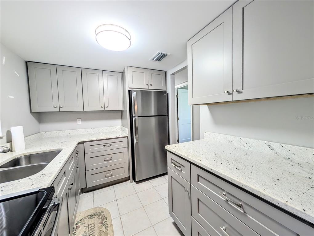 A kitchen features gray cabinets, speckled white countertops, and stainless steel appliances — 2008 CANAL DRIVE UNIT M3, BRADENTON, FL
