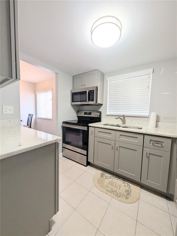 A kitchen features gray cabinets, stainless steel appliances, granite countertops, and light-colored tile flooring — 2008 CANAL DRIVE UNIT M3, BRADENTON, FL