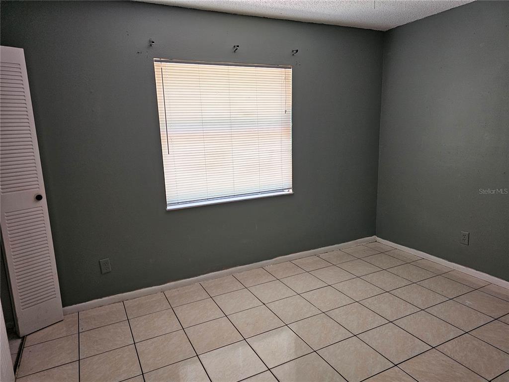 An empty room features gray walls, white tile flooring, and a window with blinds — 102 WHITEHALL WAY, KISSIMMEE, FL