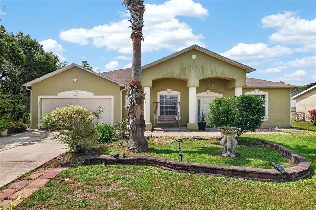 A single-story house with a green stucco exterior, a two-car garage, and a front yard — 2728 SW 153RD PLACE ROAD, OCALA, FL