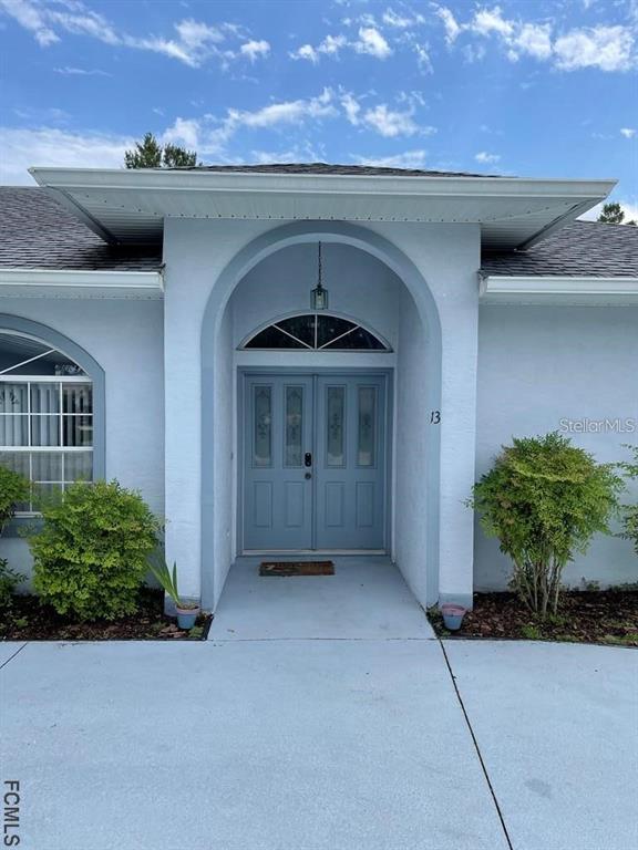 The exterior of a light blue house features a covered arched entryway with double doors — 13 FREEMONT TURN, PALM COAST, FL